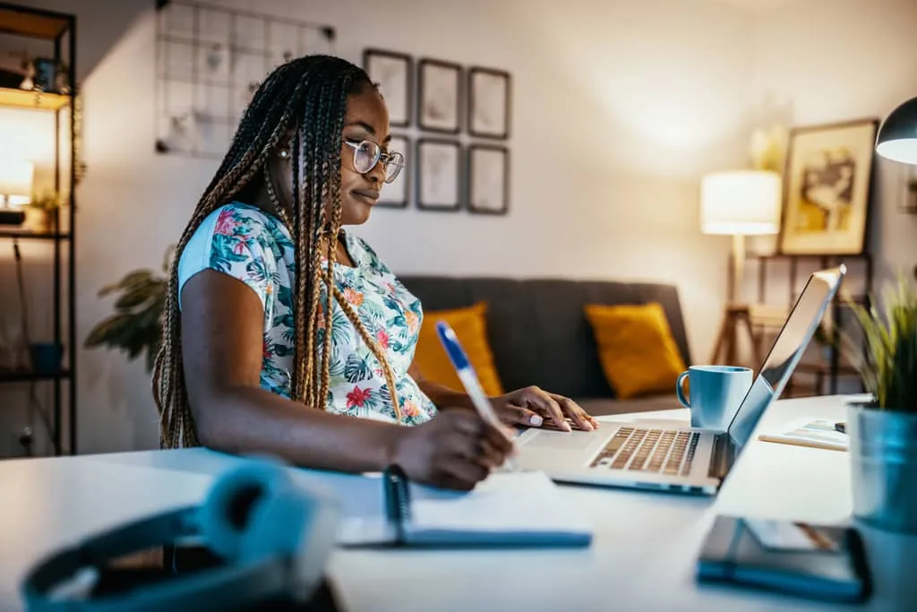 voucher process, woman with pen and notebook at her home computer.
