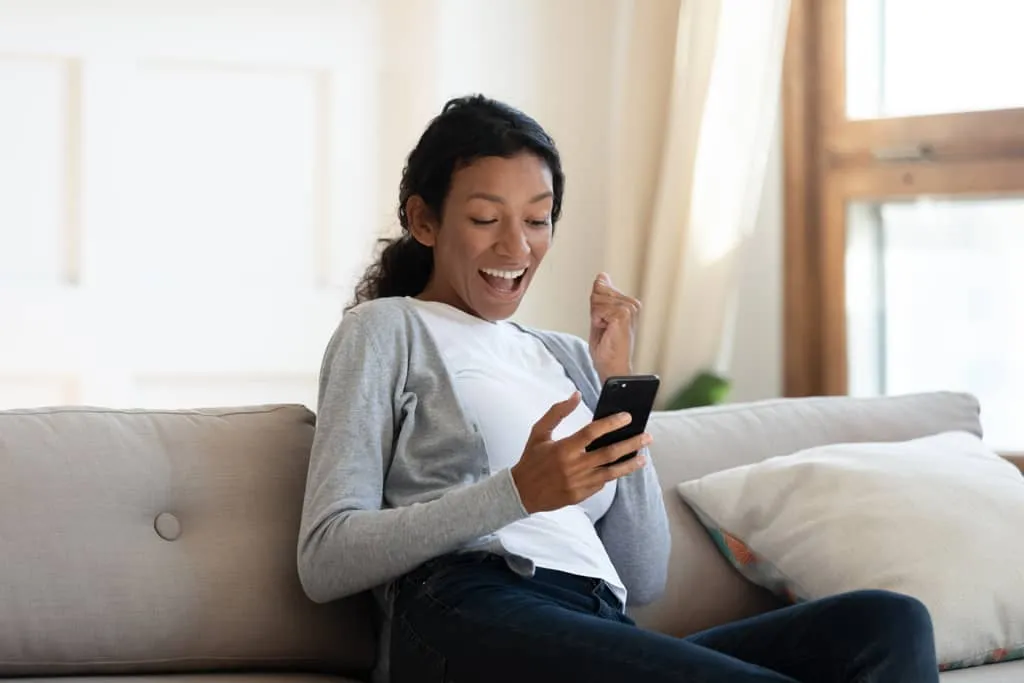 voucher process, excited woman with her phone on the couch.