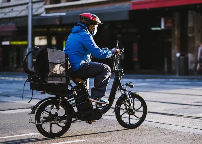 Eligibility - California E-Bike Incentive, Person driving e-bike with cargo on back rack through city streets.