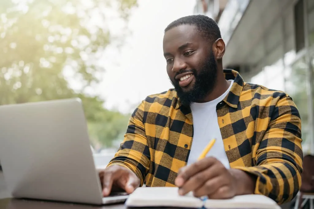 voucher process, Man with a pen and notebook outside with laptop.